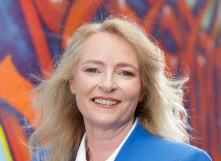 A woman smiles at the camera wearing a blue jacket and white shirt in front of a colourful wall. She is Jane Lyons, country manager for PharmaLex Ireland.