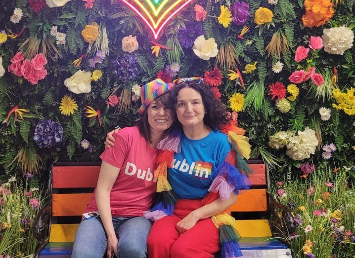 Two women dressed in colourful clothes with Dublin written on the t-shirts sitting on a bench and celebrating Pride. They are Sue Duke and Sharon McCooey of LinkedIn.