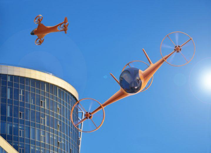 3D rendering of flying cars in an urban setting with the blue sky and sun above and a building to the side.