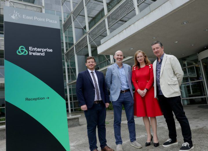 Three men and one woman stand together next to a banner with the Enterprise Ireland logo on it.