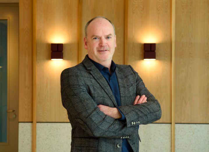 A man wearing a dark suit stands with his arms folded in a room with wood panel walls behind him. He is Gary Corley, head of cyber services at Ergo.