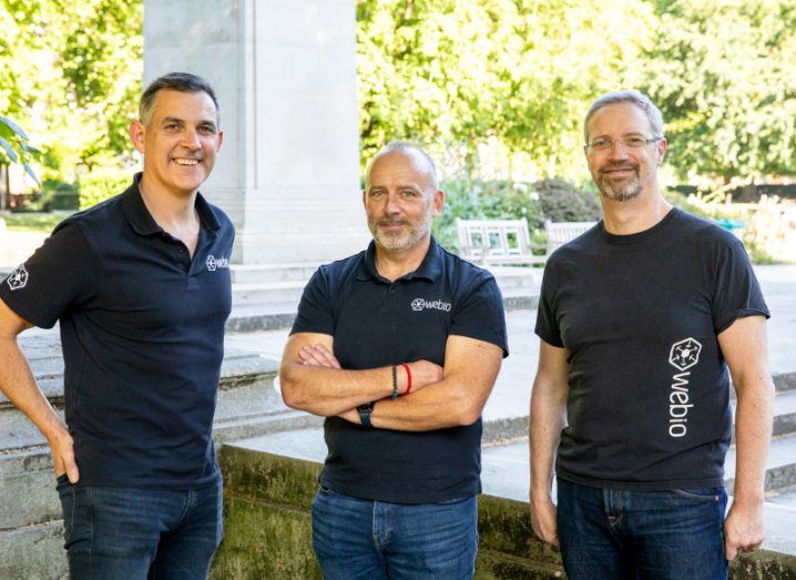 Three men standing together, each wearing black t shirts that have the Webio logo on them. They are the co-founders of Webio.