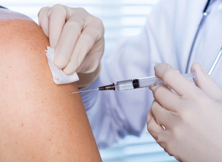 A doctor wearing white medical gloves and injecting the arm of a patient. Used to represent vaccines.