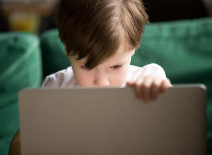 A young child looking at a laptop screen, with a green couch in the background.