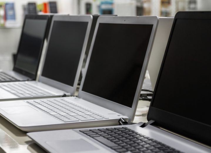 A row of laptops laying on a table, with other devices blurred in the background.