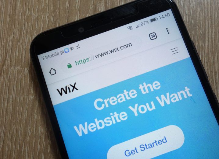 A smartphone showing the Wix website on the screen. The phone is laying on a wooden surface.