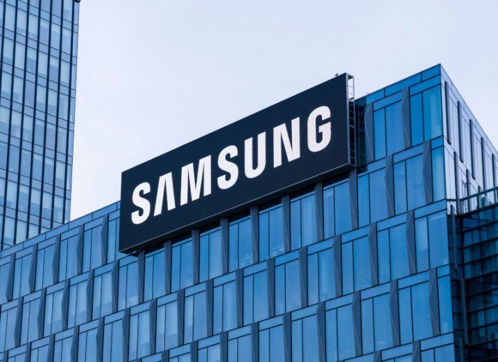 The Samsung logo on the top of a windowed building, with a grey sky in the background.