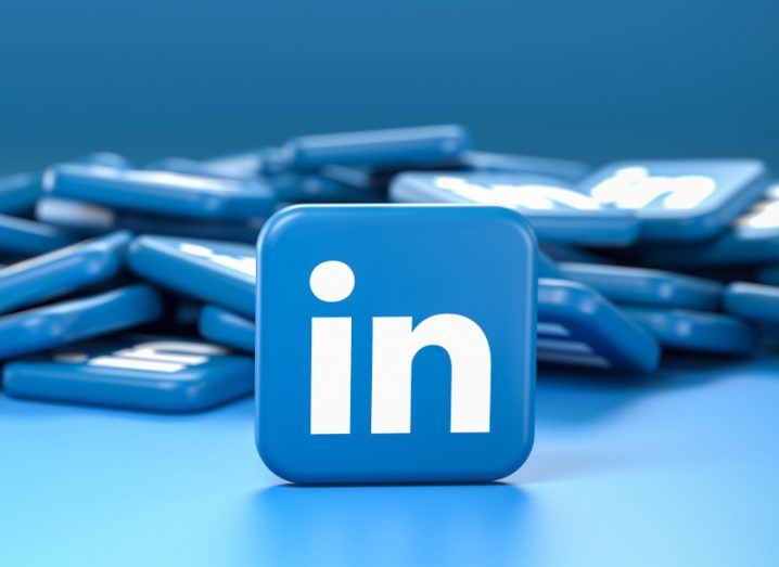 The LinkedIn logo on a blue square, in front of a pile of blue squares and standing on a blue surface.