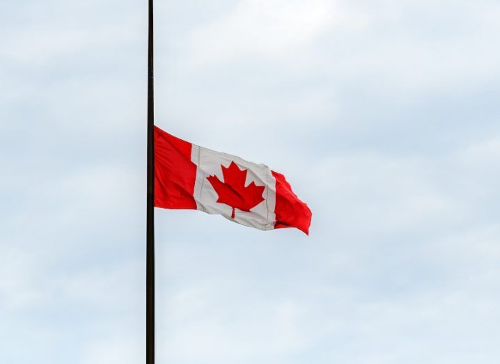 The flag of Canada on a flag pole, with a cloudy sky in the background.