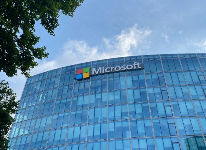 The Microsoft logo on the top of a building covered in windows, with a blue sky overhead.