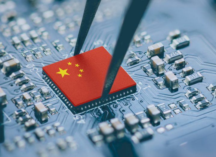 A computer chip with the China flag on it, being lifted up by a pair of tweezers.