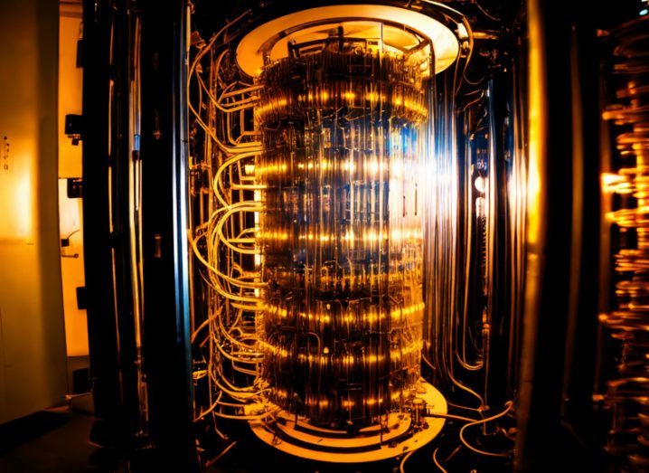 A quantum computer in a room with orange light visible on parts of the machine and cylindrical pipes surrounding it.