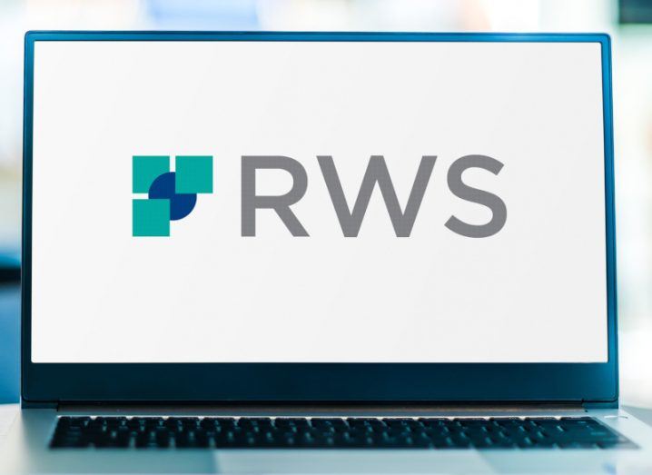 The RWS Holdings logo on a laptop screen in a blurred office background. The laptop is on a table.
