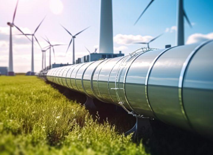 A hydrogen pipeline on a grassy field, with wind turbines in the background on a sunny day.