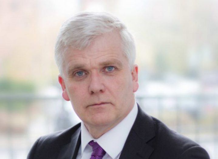 Headshot of a man in a suit with a blurred railing in the background. He is Michael Phelan of GridBeyond.