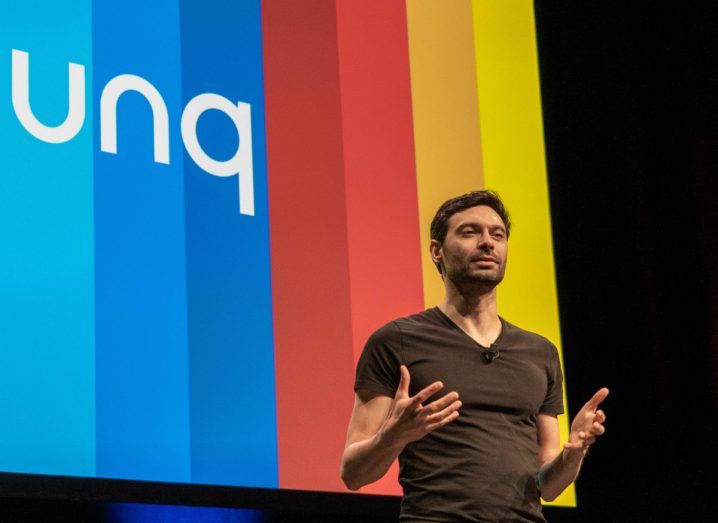 Bunq founder and CEO Ali Niknam talking to an audience from a stage. Behind him is a big rainbow-coloured screen with the Bunq logo on it.