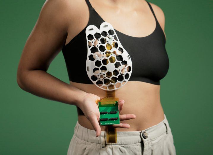 A woman holds the breast cancer ultrasound device developed by MIT in her hand. The device has honeycomb-shaped holds in it.