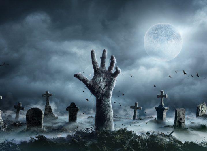 An illustration of a zombie hand coming out of a grave with headstones and a glowing moon in the background to represent zombie APIs attacking.
