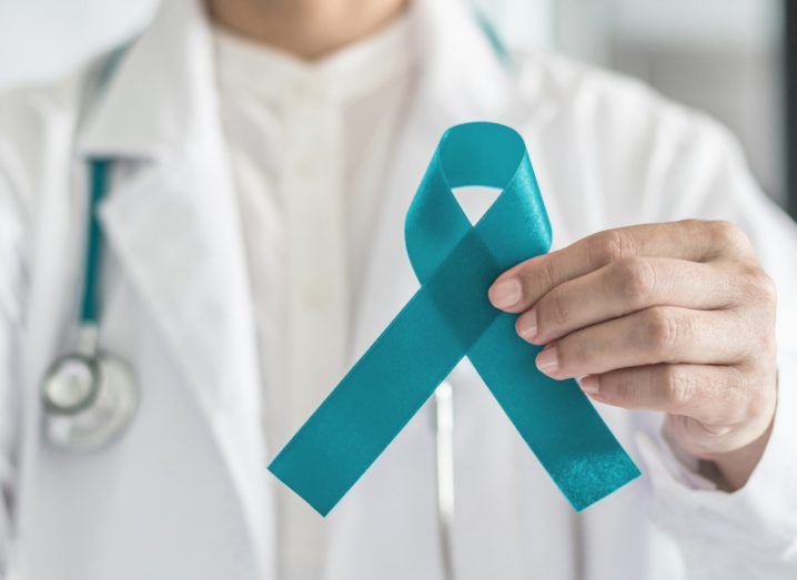 A teal coloured ribbon in a doctor's hand, used as a symbol of ovarian cancer.