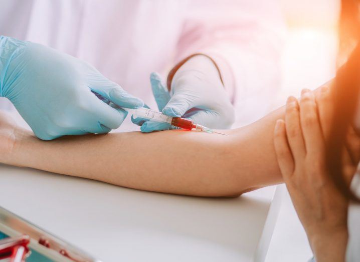 A person wearing medical gloves taking blood from a patient's arm.