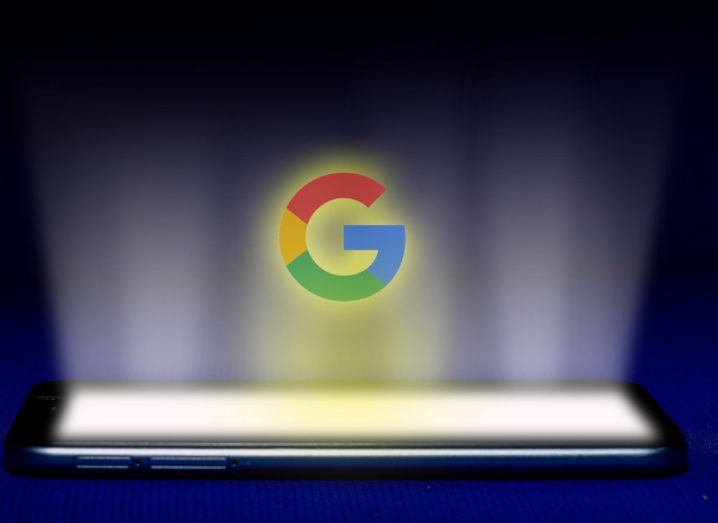 The Google logo hovering over a smartphone, with light beaming out from the screen.