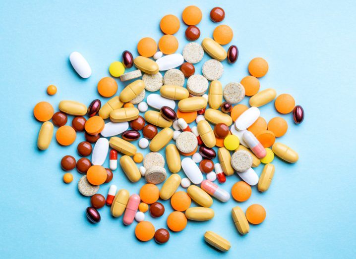 A pile of medical tablets of different sizes and colours, on a blue surface.