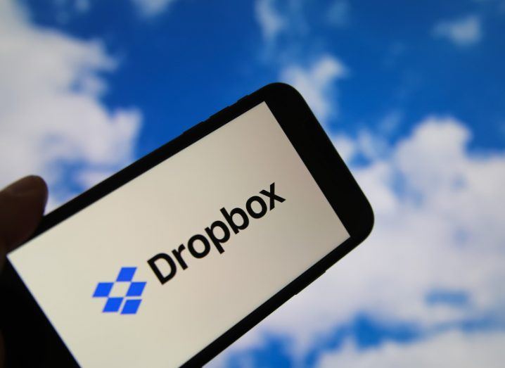 The Dropbox logo on a smartphone screen, with clouds in the background.
