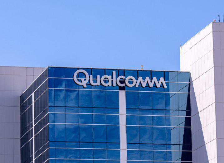 The Qualcomm logo on the top of a building, with a blue sky above it.