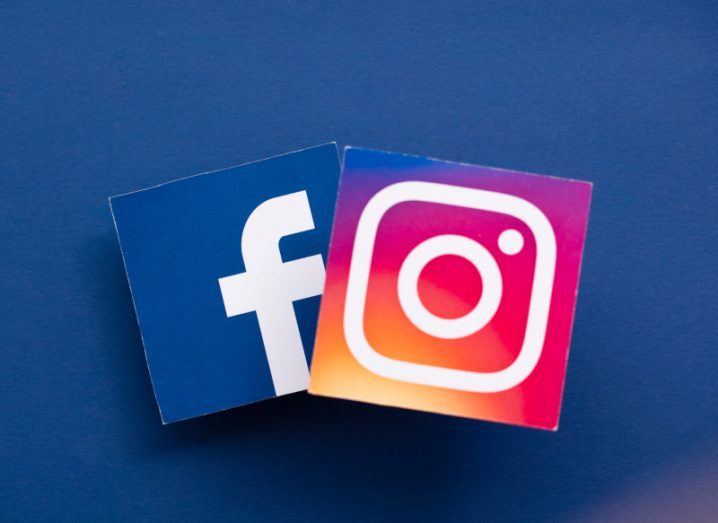Two paper logos of Meta platforms Facebook and Instagram, laying next to each other on a dark blue surface.