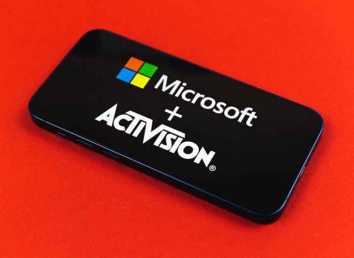 The Microsoft and Activision logos on a smartphone screen. The phone is laying on a red background.