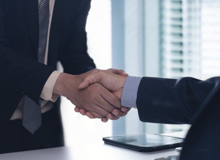 Two people in business suits shaking hands in an office.
