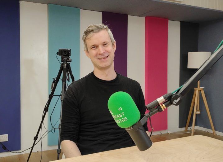 A man in a black jumper sits in a podcast studio in front of a green microphone. He is Dr David McKeown.
