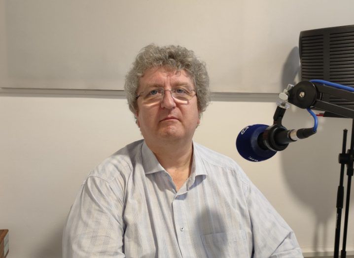 A man sits beside a podcast microphone while looking straight at the camera. He is Prof Gareth Jones.