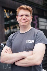 Photo of Jakob Freund from Camunda with his arms crossed. He is wearing a grey t-shirt. He has red hair and glasses and smiles at the camera.