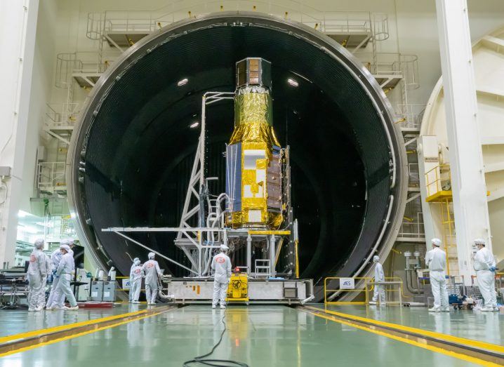 A spacecraft inside a facility with scientists wearing lab suits standing around it.