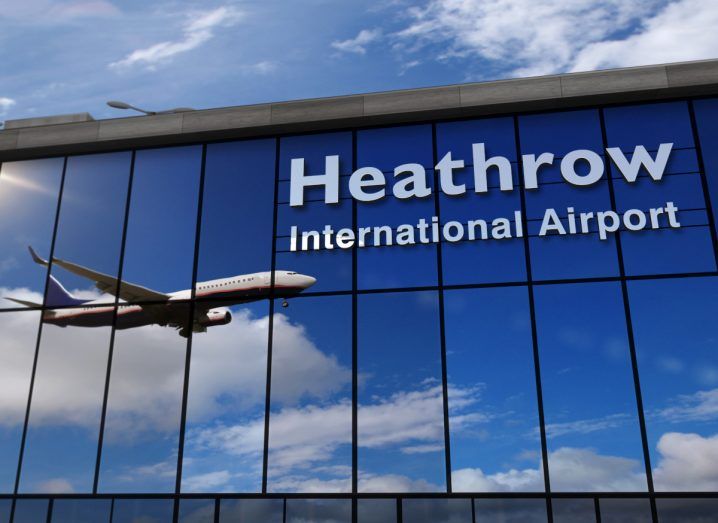 Logo of Heathrow International Airport in London shown on a glass building reflecting a flight either taking off or about to land.