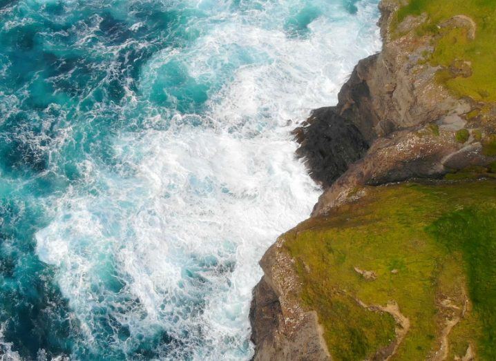 An aerial view of waves rushing up against an Irish coastline.