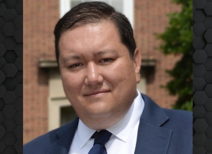 A man wearing a suit smiles at the camera with a what appears to be a red brick building behind him. He is William Alfred Rose, chief technology officer at Talent Select AI.