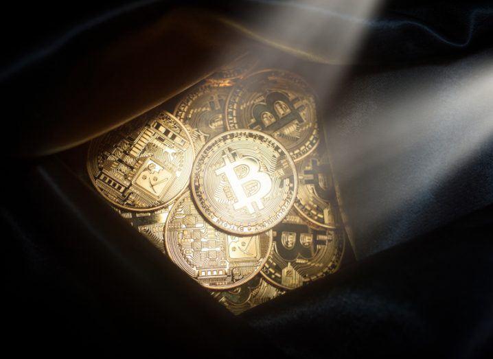 A bag containing gold coins with the bitcoin logo on them, with two spotlights shining on the coins. Used as a concept for crypto crime.