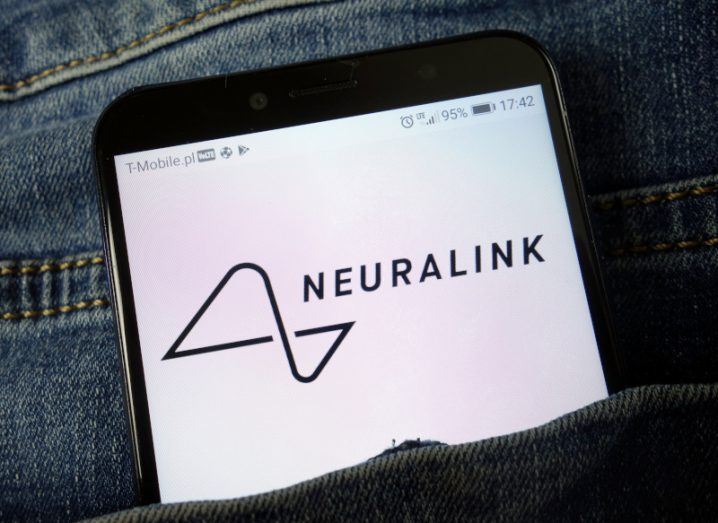 The Neuralink logo on a smartphone screen. The phone is in the pocket of a pair of jeans.
