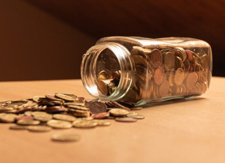 A jar full of coins turned to its side on a table, with coins spilling out.