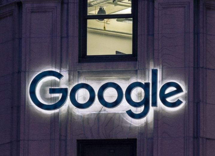 The Google logo on a building wall with a window above it.