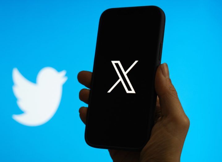 The X logo on a smartphone screen, with the Twitter logo in the background.