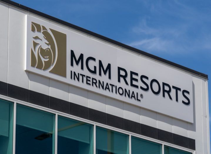 The MGM Resorts logo on the front of a grey building, with windows below it and a blue sky above.