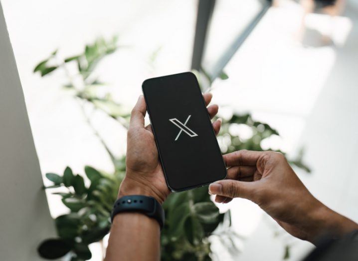 A person holding a smartphone that has the X logo on the screen.