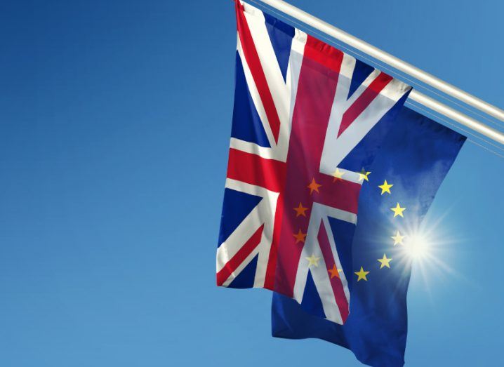The EU and the UK flag side by side tilted from the right of the picture against a bright sun.