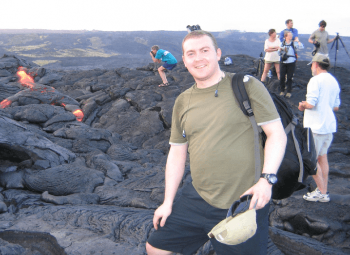A man wearing a green T-shirt and dark shorts with a backpack slung over his shoulder smiles in front of a lava flow. He is Richard Morrell, CTO at My1Login.