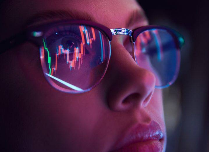 Photo of a woman wearing glasses and staring at a computer screen. The glasses are reflecting light from the computer screen,