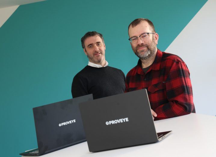 Two men sitting behind a table with laptops on top. The laptops have the Proveye logo on them.