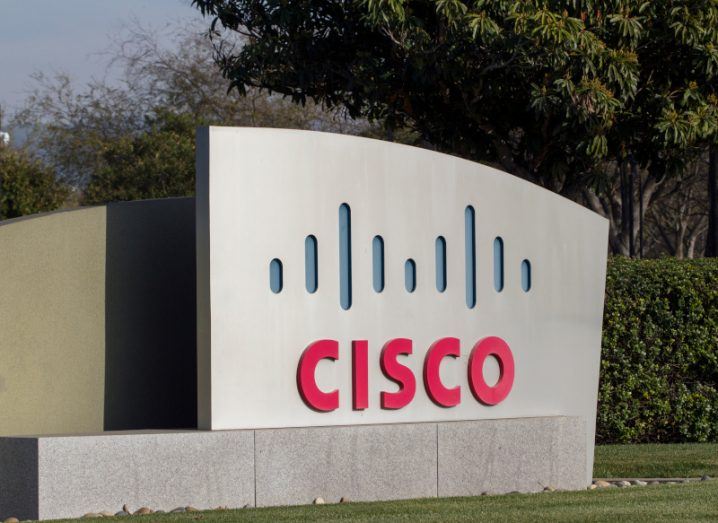 A picture of Cisco's sign outside of its corporate campus in Milpitas, California. There are trees and shrubbery behind the sign.